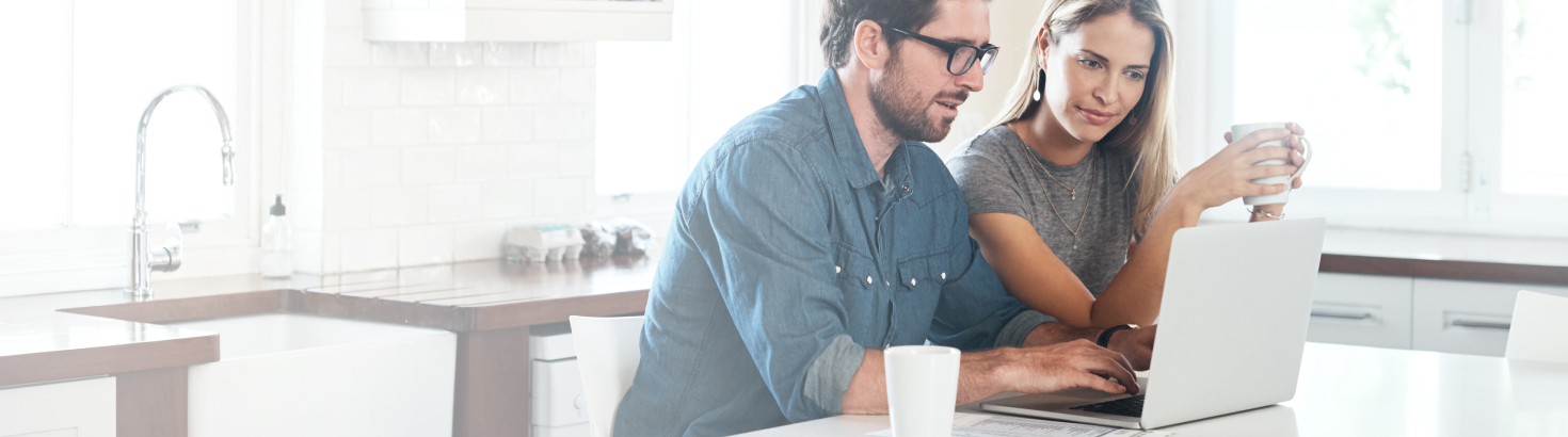 A young couple sitting in their kitchen using a laptop